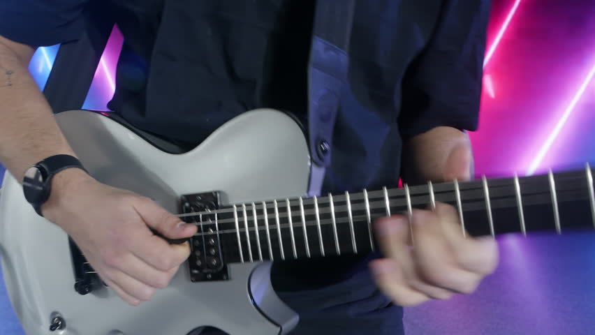 Male musician playing white electric guitar, intense neon lighting highlighting dynamic performance, capturing raw energy of rock music through close up of passionate guitarist's hands