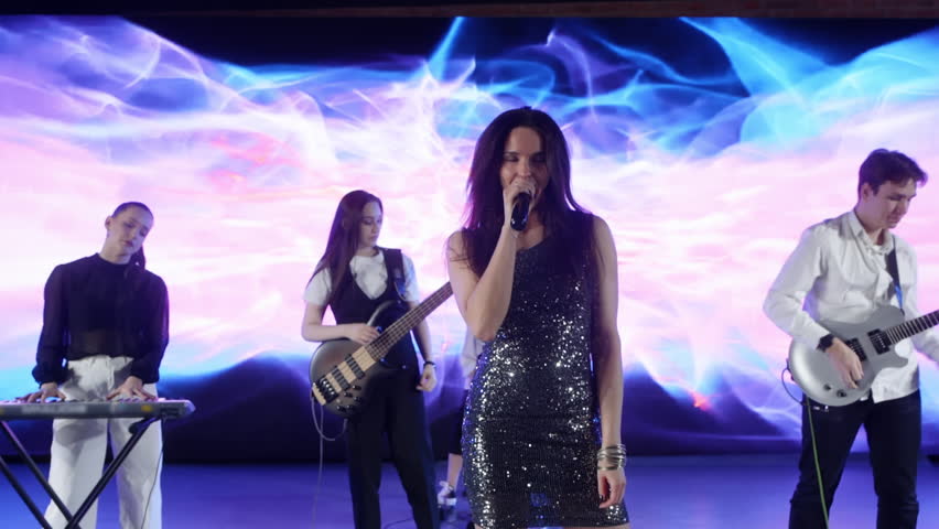 Vibrant music band performing passionately on stage, energetically playing instruments and singing against dynamic led wall displaying colorful abstract animations