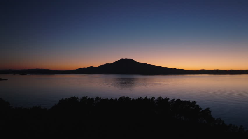 Drone gliding across the waters on the Norwegian coast after dark, revealing glowing reflections of the sunset sky