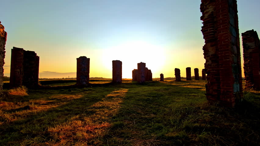 Ruins of ancient brick columns in grassy field during scenic sunrise in silence