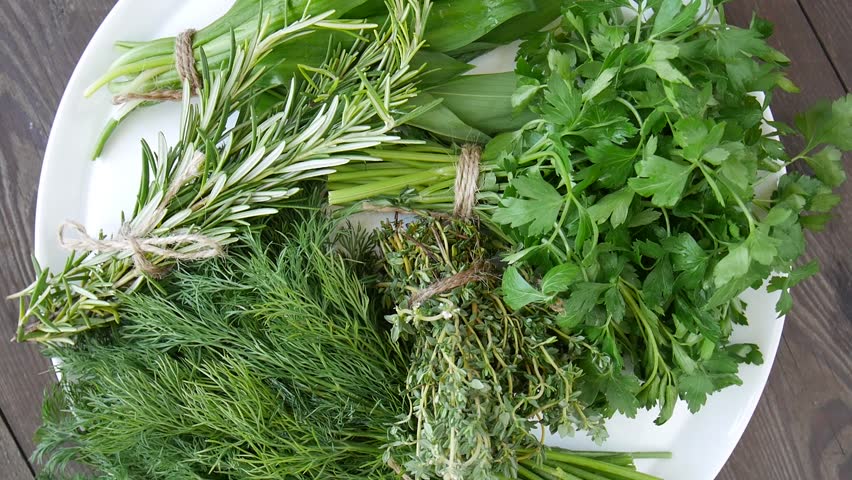 Freshly harvested herbs, tied in bunches, rotate slowly on a white plate.