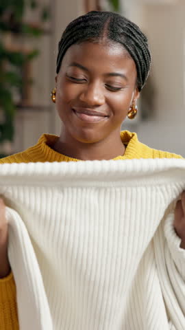 Smelling, laundry and black woman in home for housekeeping, maintenance or spring cleaning. Happy, fabric and African female person with scent on material of clothes in living room at apartment.