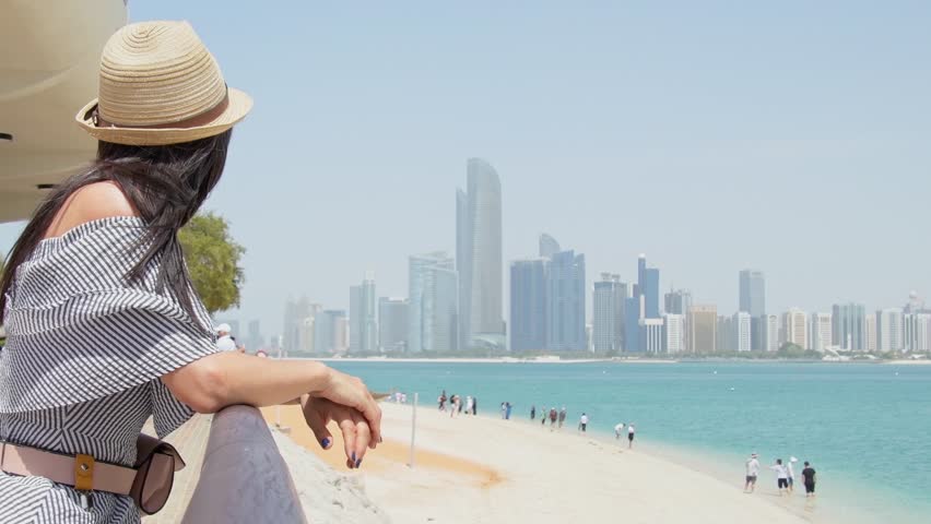 Woman tourist on viewpoint admire picturesque panorama of sandy turquoise water beach with tourist group. Abu dhabi metropolis skyline background. Traveler enjoy holidays explore emirates and gulf