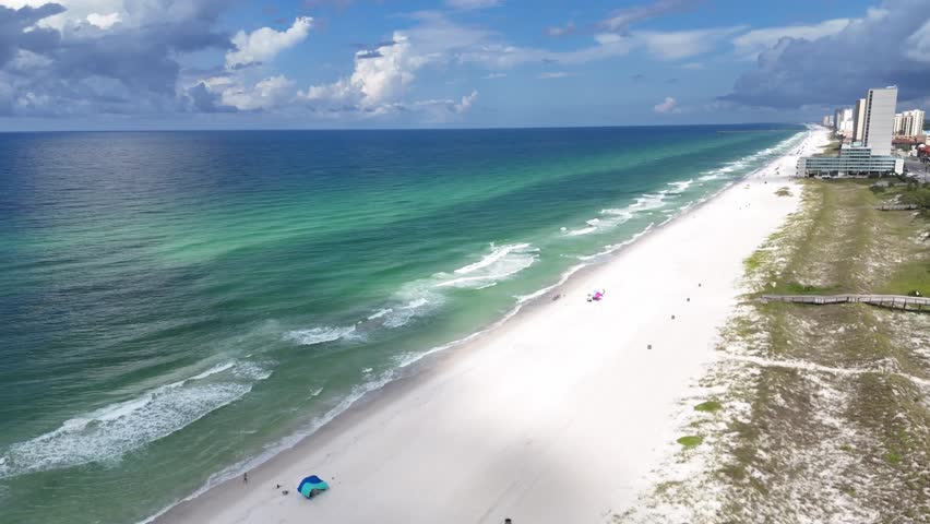 Panoramic orbiting drone fly over the white sandy beach with turquoise ocean waves and coastal buildings, Panama City Beach, Florida, USA