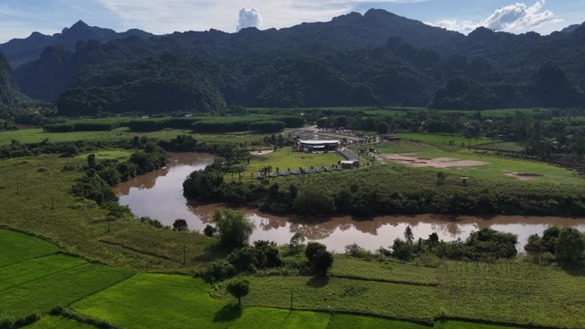 Aerial footage of a muddy river flowing through a lush green valley and rural landscape in Southeast Asia.