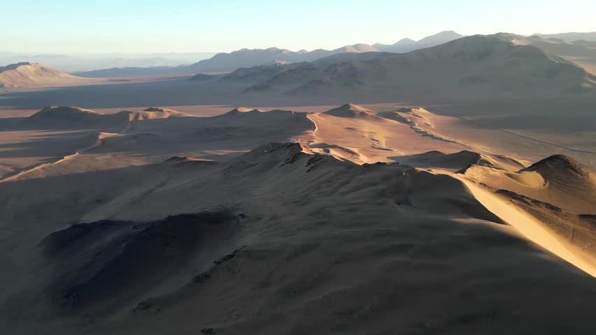 Sweeping drone shot of sand dunes in Chile’s Atacama Desert, the evening light painting soft highlights across its wind-sculpted curves.