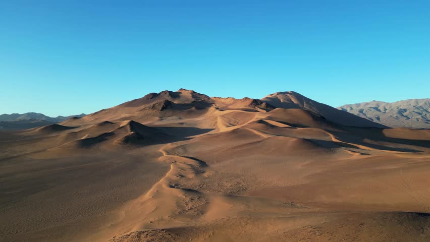 Aerial drone shot of the Chilean Atacama Desert’s dramatic dunes drenched in evening golden light.