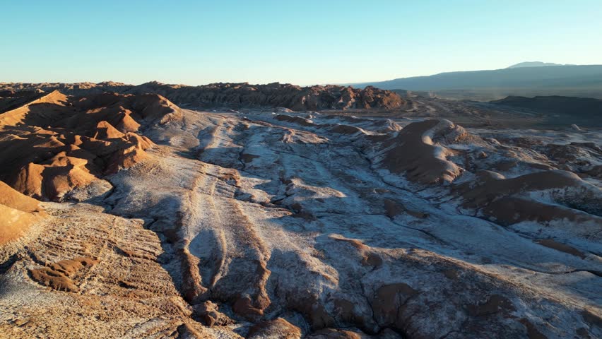 Aerial drone shot of Valle de la Luna at sunset, with jagged desert rock formations glowing in golden light.