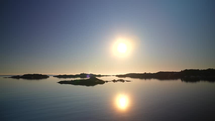 Artic Circle golden hour sunset sunrise sun flare on horizon reflection Norway Sweden coastline islands Hovedøya Sandefjord Strömstad Oslofjord ferry boat ride costal seaside town winter pan follow