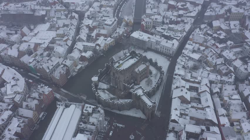 Aerial view of the snow-covered Gravensteen Castle surrounded by a moat and buildings with snow covered roofs, Ghent, Flanders, Belgium.