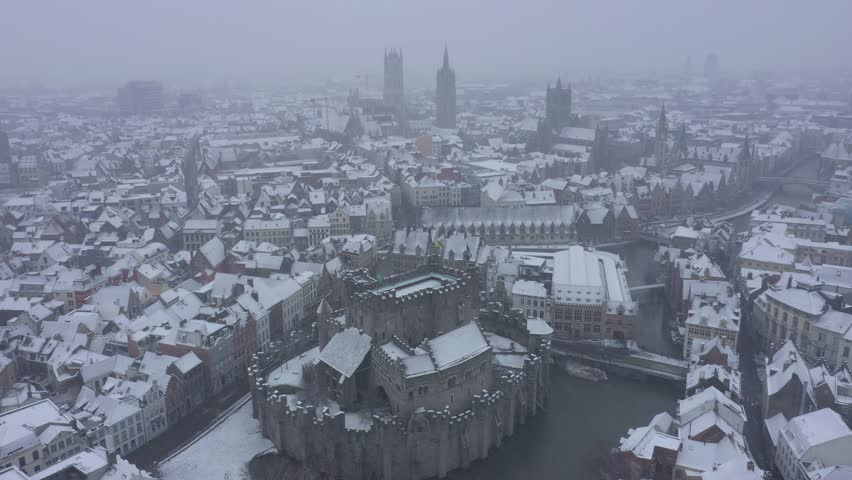 Aerial view of the snow-covered Gravensteen castle encircled by a moat, with rooftops and buildings dusted with snow creating a monochromatic scene, Ghent, Flanders, Belgium.