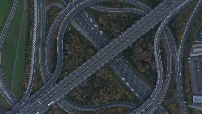 Aerial view of a complex highway interchange featuring curved ramps and multiple lanes cutting through the landscape, Ghent, Flanders, Belgium.