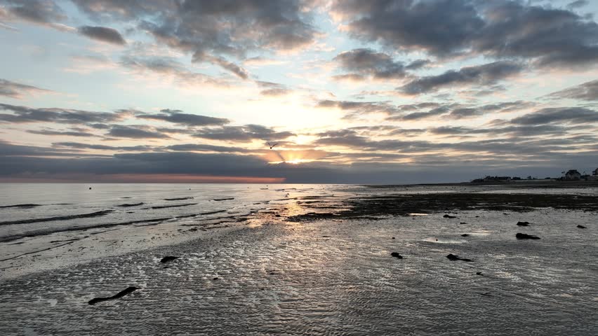 Aerial view of low tide revealing textures and patterns on the beach, with the sun setting behind the clouds, Bernières-sur-Mer, Normandy, France.