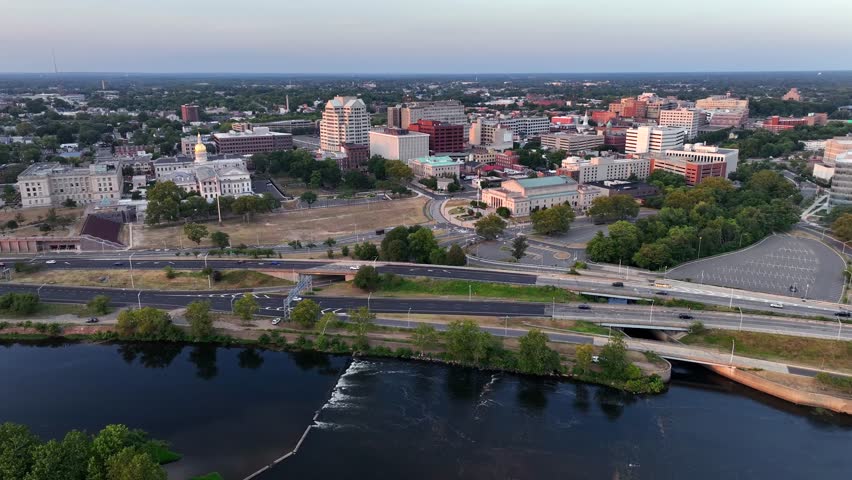 Traffic on coastal road in front of Trenton Downtown at sunrise. Descend drone wide shot. Summer day in New Jersey. High-rise buildings and offices in district. Financial area.