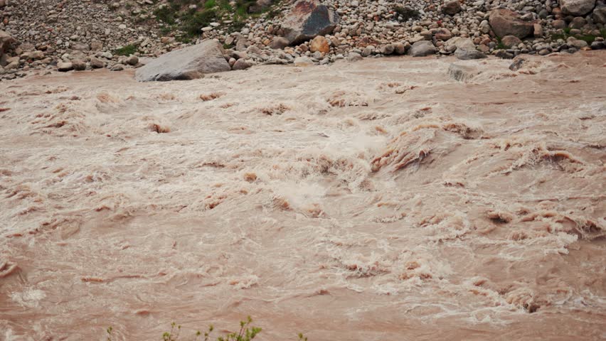 4K Slow motion shot of Beas River in full flood in Mandi, Himachal Pradesh, India. Flood in Himalaya mountains after heavy rain in monsoon season. Flood water fast flowing down swollen mountain.
