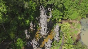 Aerial view circles a colossal Hindu statue framed by dense greenery in a riverside temple in Bali, Indonesia. Morning light highlights relief, revealing worship activity and cultural heritage - Powered by Shutterstock - Get 15% off with code: PIKWIZARD15