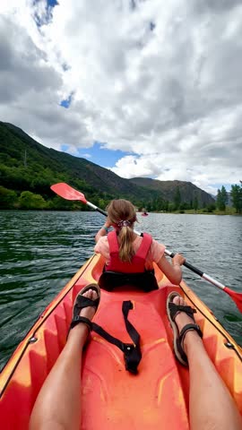 Young girl paddling a kayak on a calm mountain lake, enjoying a sunny day surrounded by nature