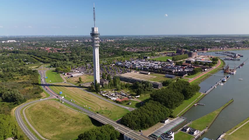 A tall communication tower rises above a riverside city with canals, bridges, boats, and green landscapes, blending modern infrastructure with natural surroundings.