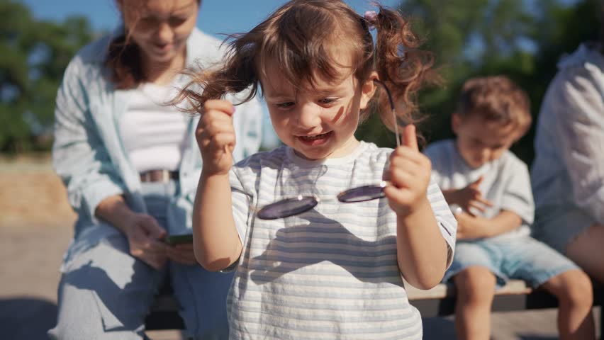 Little girl wearing sunglasses. A child is sitting outdoors with a girl. A family playing casual in the daytime. A young girl with sunglasses on lifestyle.