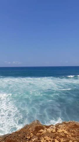 Yogyakarta, 02 August 2025: Ocean waves crash against rocky shoreline at Watu Kodok Beach, Gunungkidul, under clear blue sky. A serene tropical seascape from Yogyakarta’s south coast.
