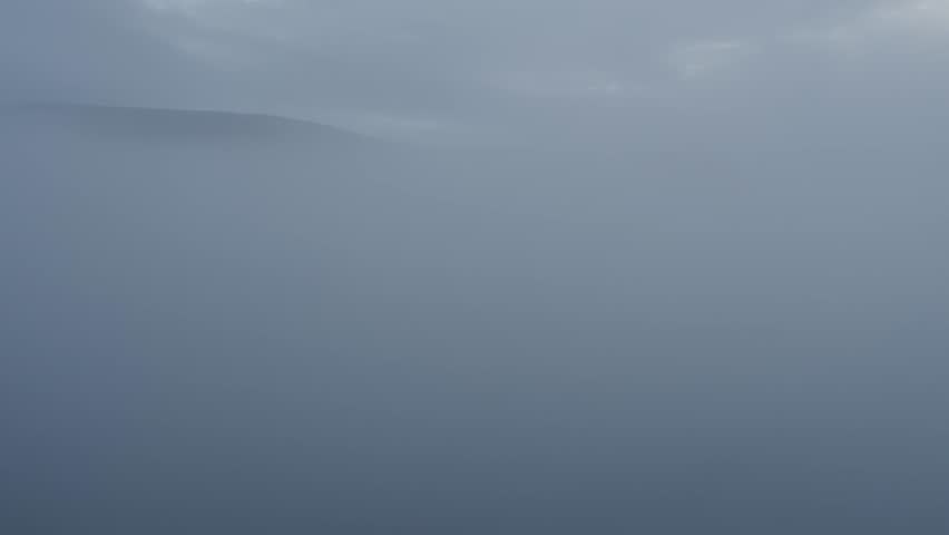 The camera emerges from the thick clouds, a view of a mountain peak