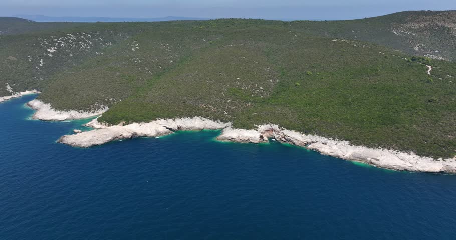 Rocky white shoreline with turquoise water coves and dense green forested hills near Dugi Otok, Croatia. Panoramic drone aerial