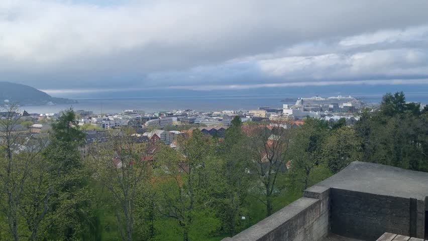 Panoramic view of Trondheim city center, Norway, on a cloudy spring day, highlighting colorful houses and the calm fjord waters beneath an overcast sky
