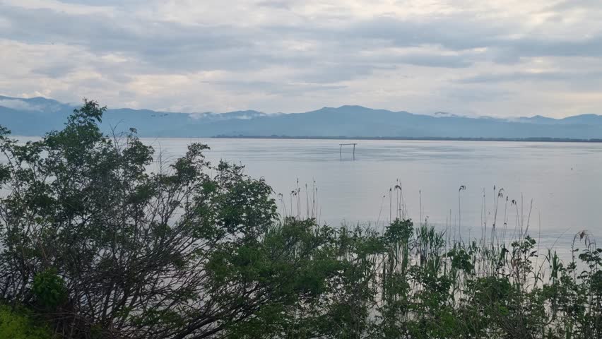Scenic view of Kerkini Lake in northern Greece on a calm, cloudy spring day, showcasing wetlands, tranquil waters, and the surrounding natural landscape