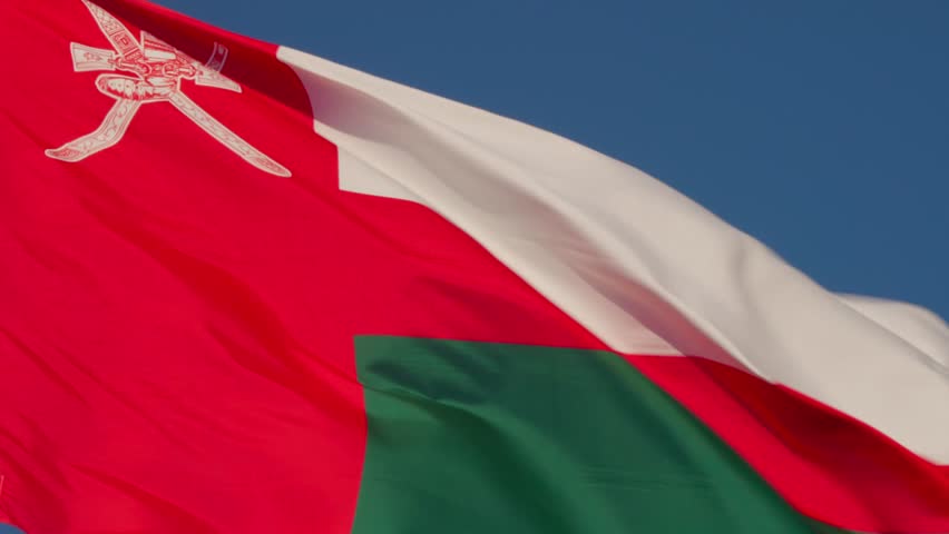 Flag of Oman featuring national emblem and horizontal red, white, and green stripes waving close-up. Location: Muscat, Oman