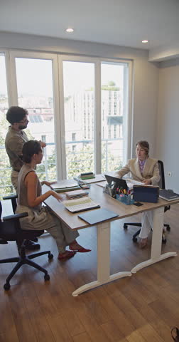 A young couple meets with a female bank representative, carefully reviewing documents to secure credit or a loan. They are discussing important financial decisions in a modern office setting.