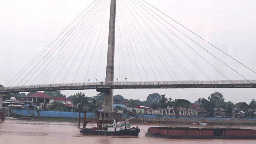Jambi, Indonesia - August 15, 2025 - Two ships pulling and pushing a boat consisting of coal in the Batanghari River while passing under the Gentala Arasy bridge