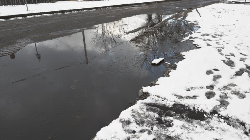 A large puddle on the road against the background of snow in winter during a thaw, snowbreak