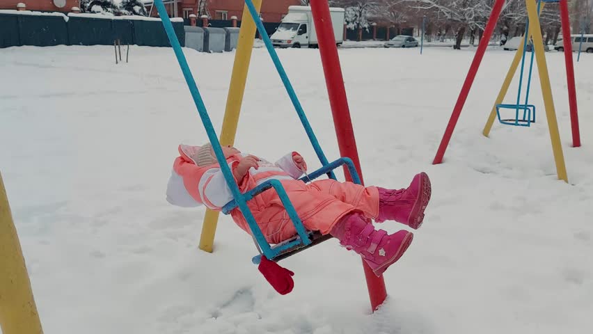 little cauacasian girl riding on a swing in winter during snowfall