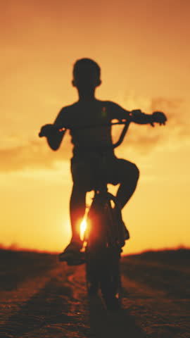 Preschooler resting in country in summer vacation, little boy riding bike, silhouette against sky in sunset. Happy childhood moments, children game in nature, leisure and entertainment, sport activity