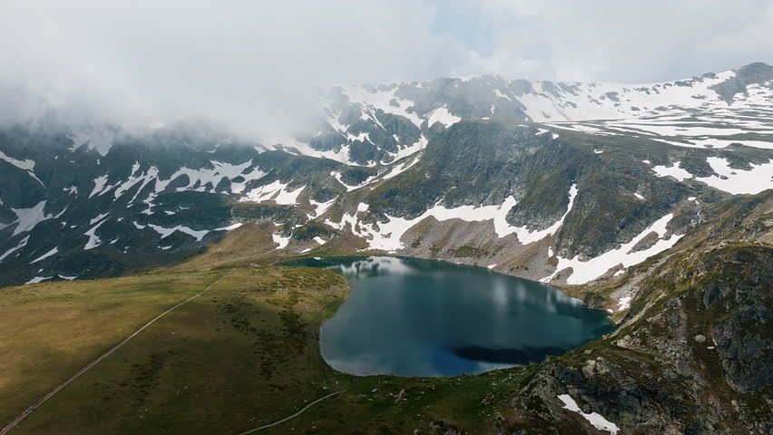 Bulgarian mountain lake scene from drone above Seven Rila Lakes, showing icy patches, dramatic slopes, tranquil water under clouds, strong for buyers seeking Eastern Europe mountain travel content