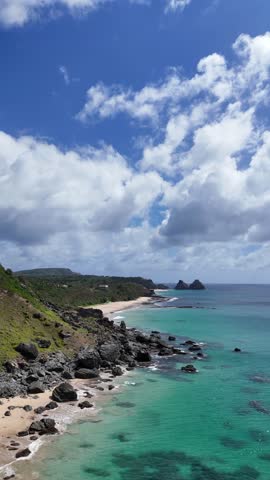 Vertical aerial view of Praia do Boldró in Fernando de Noronha, showing waves, sandy beach, cliffs, and clear waters, capturing the island’s natural coastal charm from above