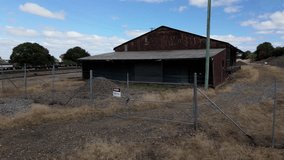 An abandoned industrial shed with a corrugated roof and rusted exterior stands fenced off beside a railway line. A "Danger Asbestos" warning sign is displayed on the locked gate. - Powered by Shutterstock - Get 15% off with code: PIKWIZARD15
