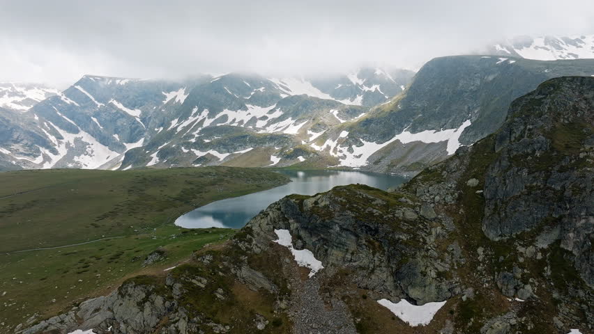Beautiful Bulgarian mountain lake scene from drone above Seven Rila Lakes, showing icy patches, dramatic slopes, tranquil water under clouds, strong for buyers seeking Eastern Europe mountain travel 