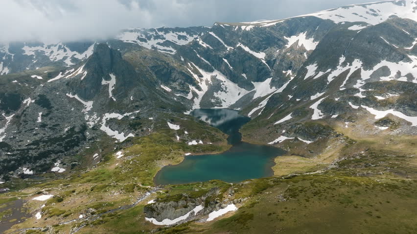 Epic aerial shot of Seven Rila Lakes National Park in Bulgaria capturing snow-covered peaks, blue water, steep cliffs, popular among tourists adventurers searching for Balkan summer mountain landscape