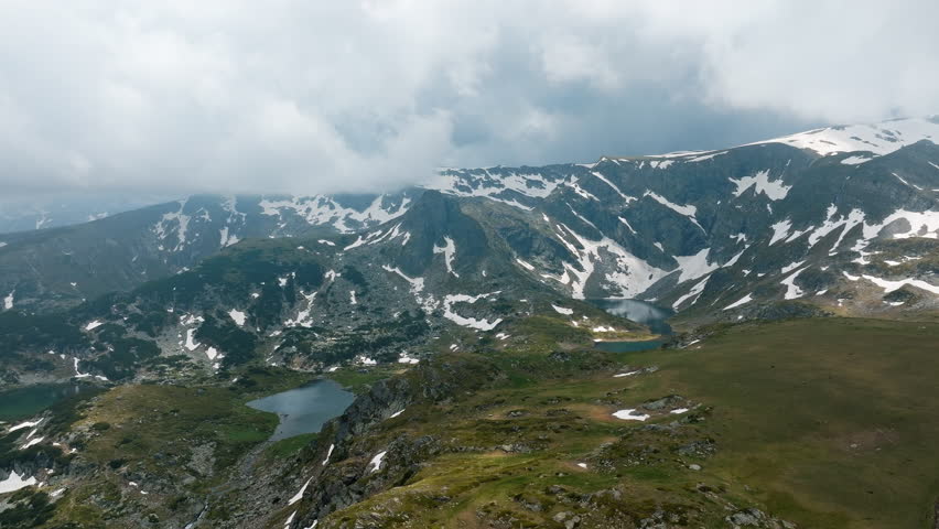 Stunning mountain scene at Seven Rila Lakes Bulgaria featuring snow patches, deep blue lake, rocky ridges under foggy sky, captured by drone for hiking, nature, adventure, aerial, and Balkan mountain 