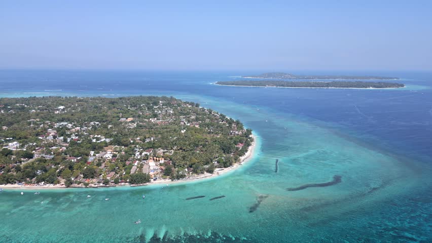Aerial view of Gili Air island, Indonesia, with Gili Meno and Gili Trawangan visible in the background. Scenic tropical seascape with turquoise water and coral reefs.