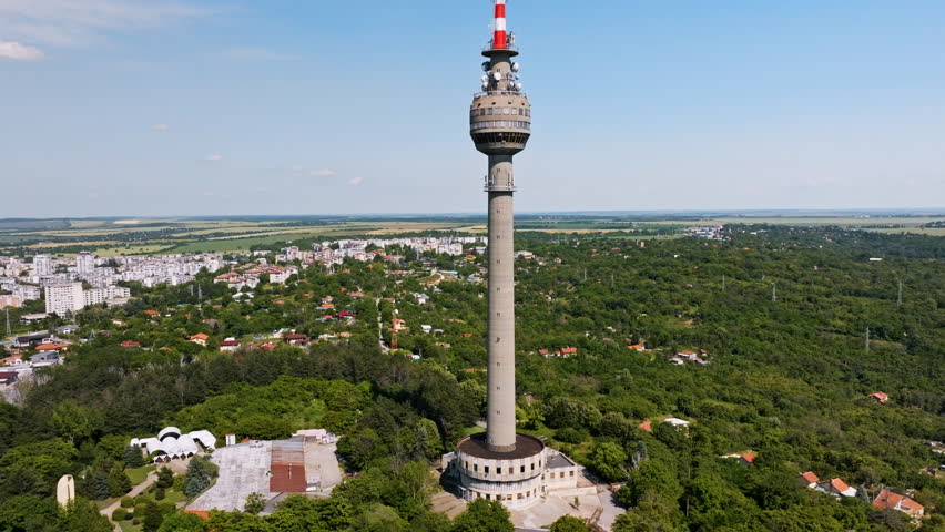 Travel drone shot Ruse Bulgaria high telecommunications tower above green urban forest and city, representing modern broadcasting infrastructure, tourism development, unique Balkan architecture