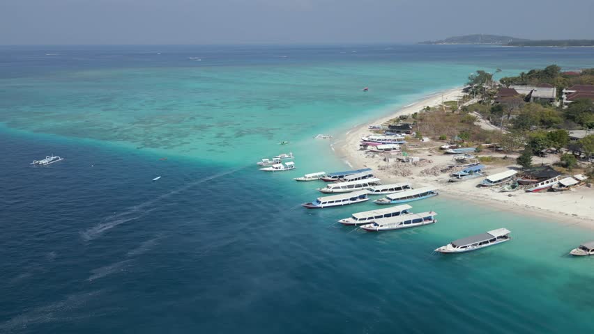 Aerial view of Gili Air island, Indonesia, with boats docked along the tropical shoreline. Clear turquoise waters, coral reef, and exotic island scenery, perfect for tourism and travel content.
