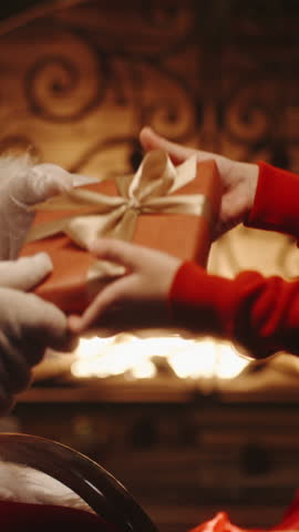 Santa Claus hands gift to child by fireplace, Christmas magic and holiday giving concept, vertical slow motion