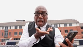 Man in formal attire seated outdoors interacts with smartphone, sharing thoughts in a relaxed atmosphere - Powered by Shutterstock - Get 15% off with code: PIKWIZARD15
