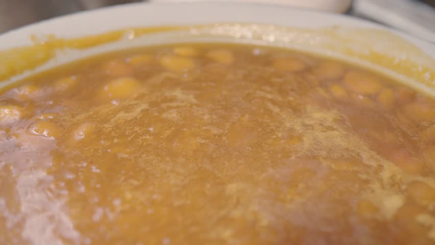 Golden-hued split pea soup fills the frame, bubbling gently. Broth is thick, speckled with softened peas. Subtle steam rises, creating a blurred effect. Bowl