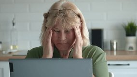 Elderly woman experiencing a headache while working on laptop, touching her temples and adjusting her glasses, showing signs of stress and fatigue in her home office. Sharp pain in head from migraines - Powered by Shutterstock - Get 15% off with code: PIKWIZARD15