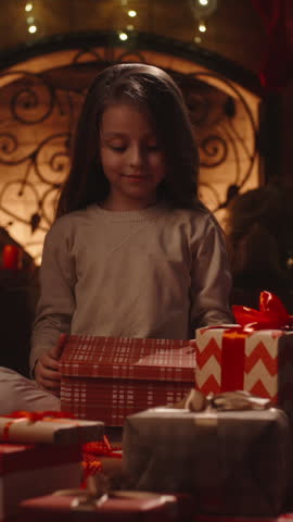 Little girl opening Christmas gift box with magical light by the fireplace