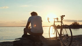 Cyclist resting during peaceful sunset moment, sitting on sandy beach with bicycle, enjoying serene ocean landscape during golden hour - Powered by Shutterstock - Get 15% off with code: PIKWIZARD15