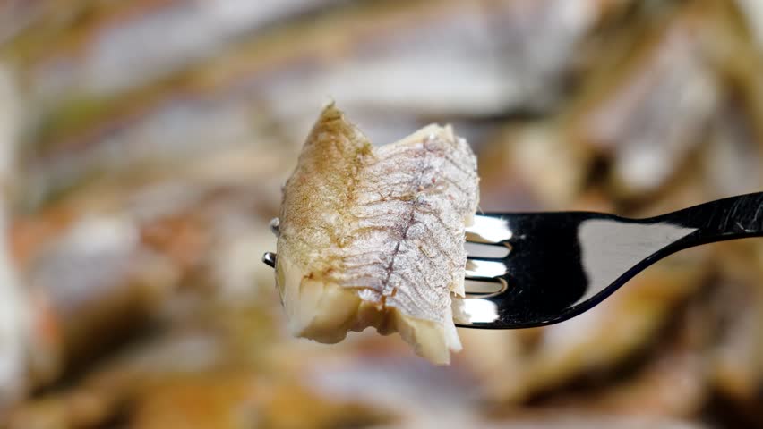 Piece of fried blue whiting fish on steel fork. Prepared seafood